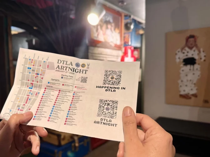 A person holds up a map with QR codes and text that reads "DTLA Artnight" in a gallery.