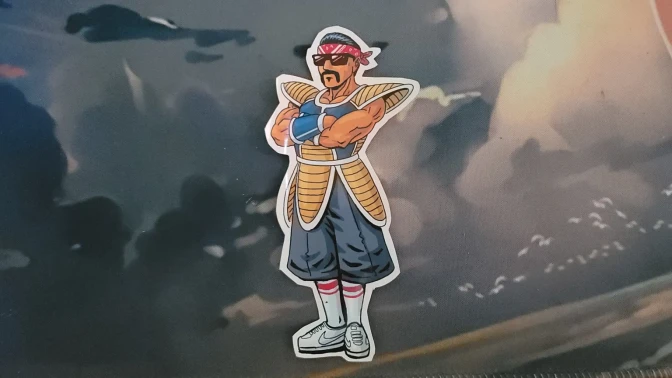 A sticker-like art piece on display of a cartoon depicting a man with medium skin tone wearing a Saiyan battle suit from the Dragon Ball series.