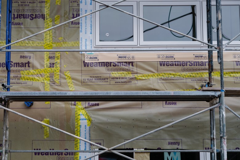A detailed look of scaffolding that sits in front of a weather-resistant barrier e of an apartment complex under construction.