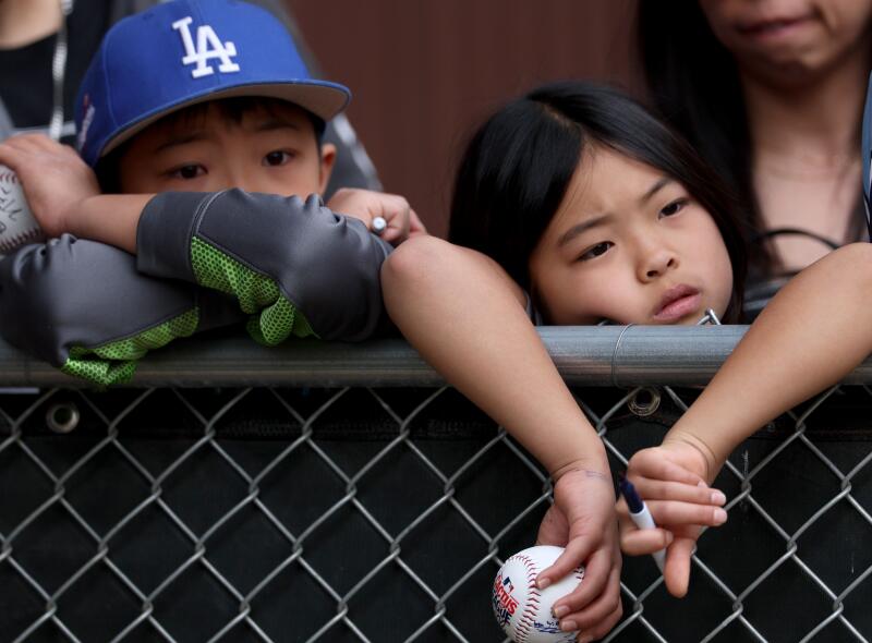 Children lean against a fence and wait to greet players during Dodgers spring training at Camelback Ranch.