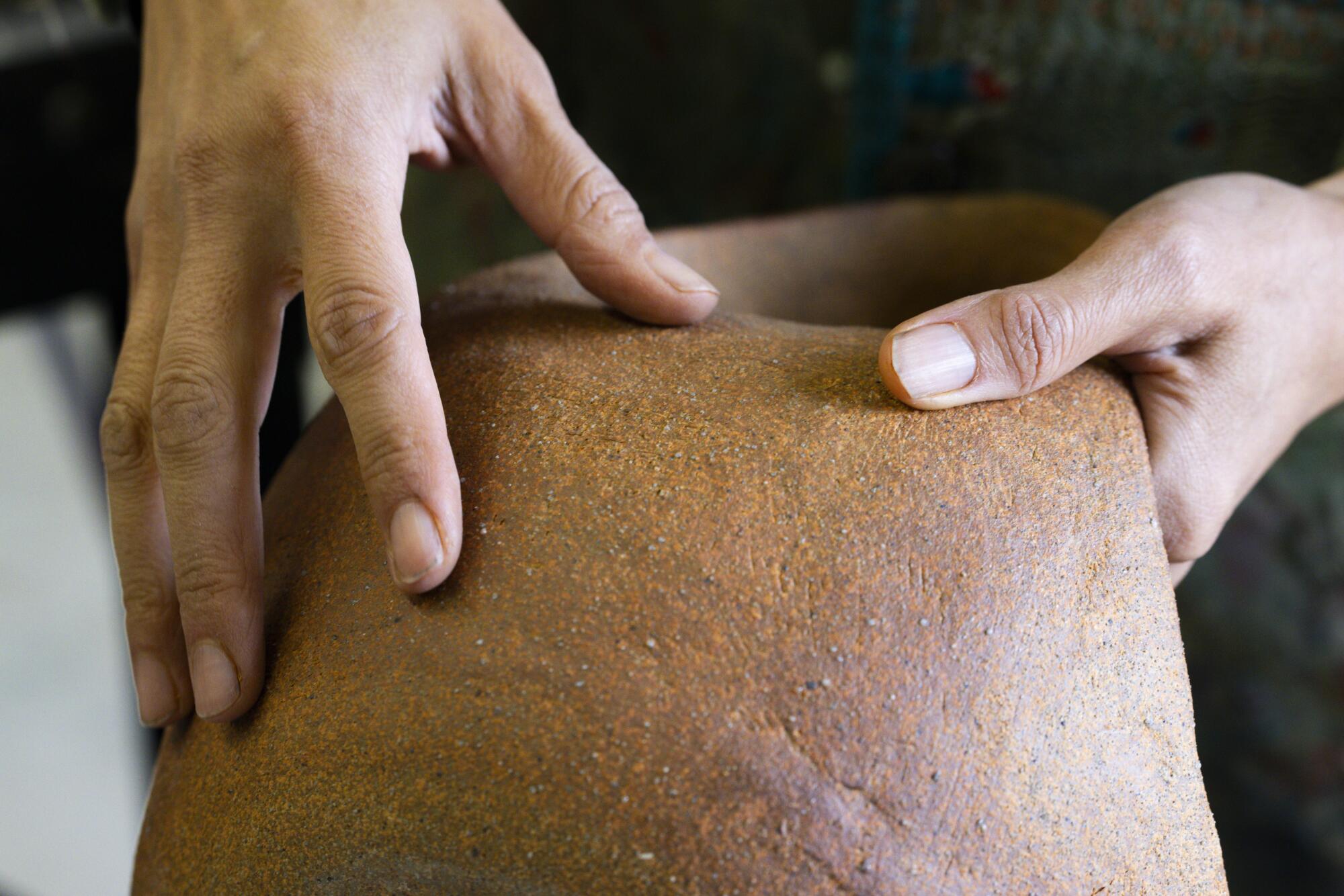 Hands touch an eathen-colored sculpture.