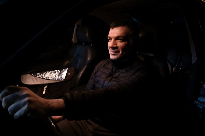 A man with light skin tone sits behind the wheel of his Mercedes Benz.