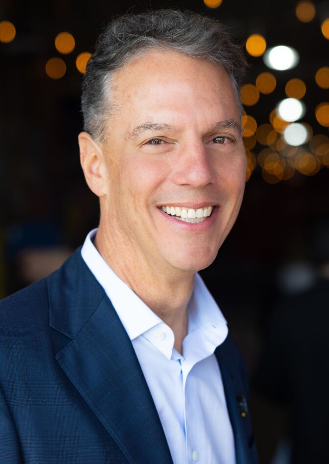 A man in a white shirt and blue sport coat smiles at the camera.