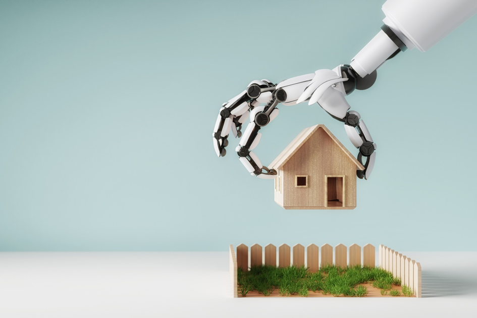 A robotic hand is holding a small wooden house above a fenced patch of grass against a light blue background.