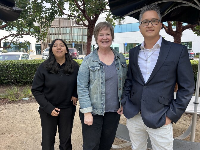 Two women and a man pose for a photo in a courtyard of an office park with buildings in the background.