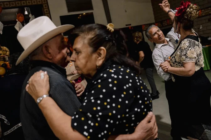 People dance together in an auditorium room with decorations on the walls and tables in the background.