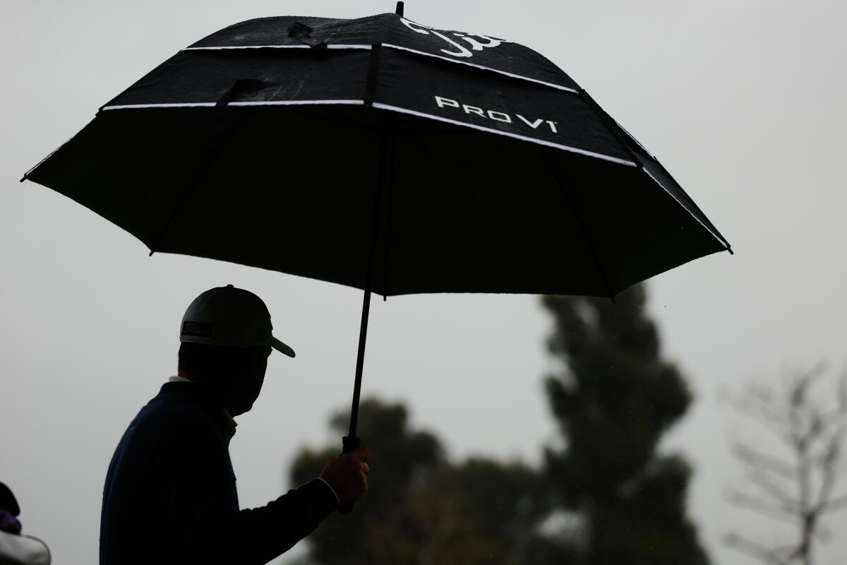 Tom Hoge carries an umbrella in the rain on the eighth hole during the first round of the Genesis Invitational.