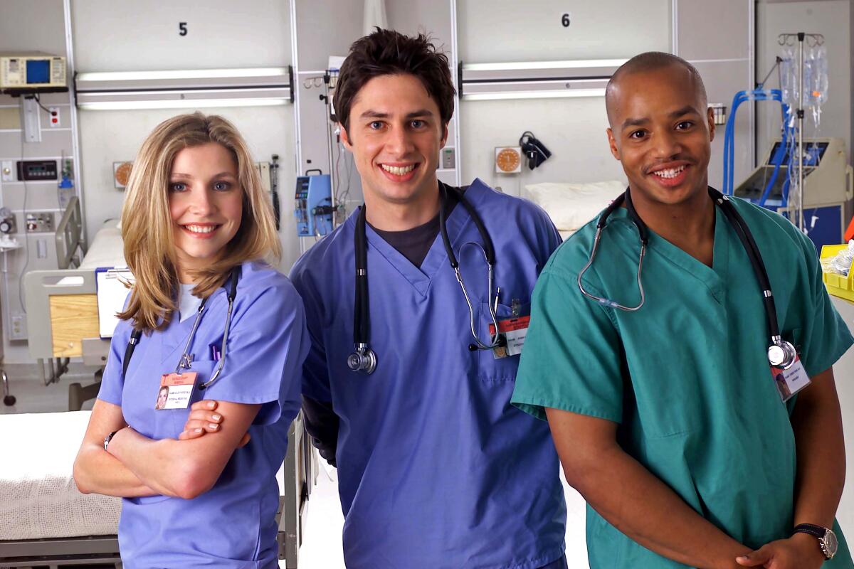 A woman and two men in blue and green medical scrubs standing in a hospital room.