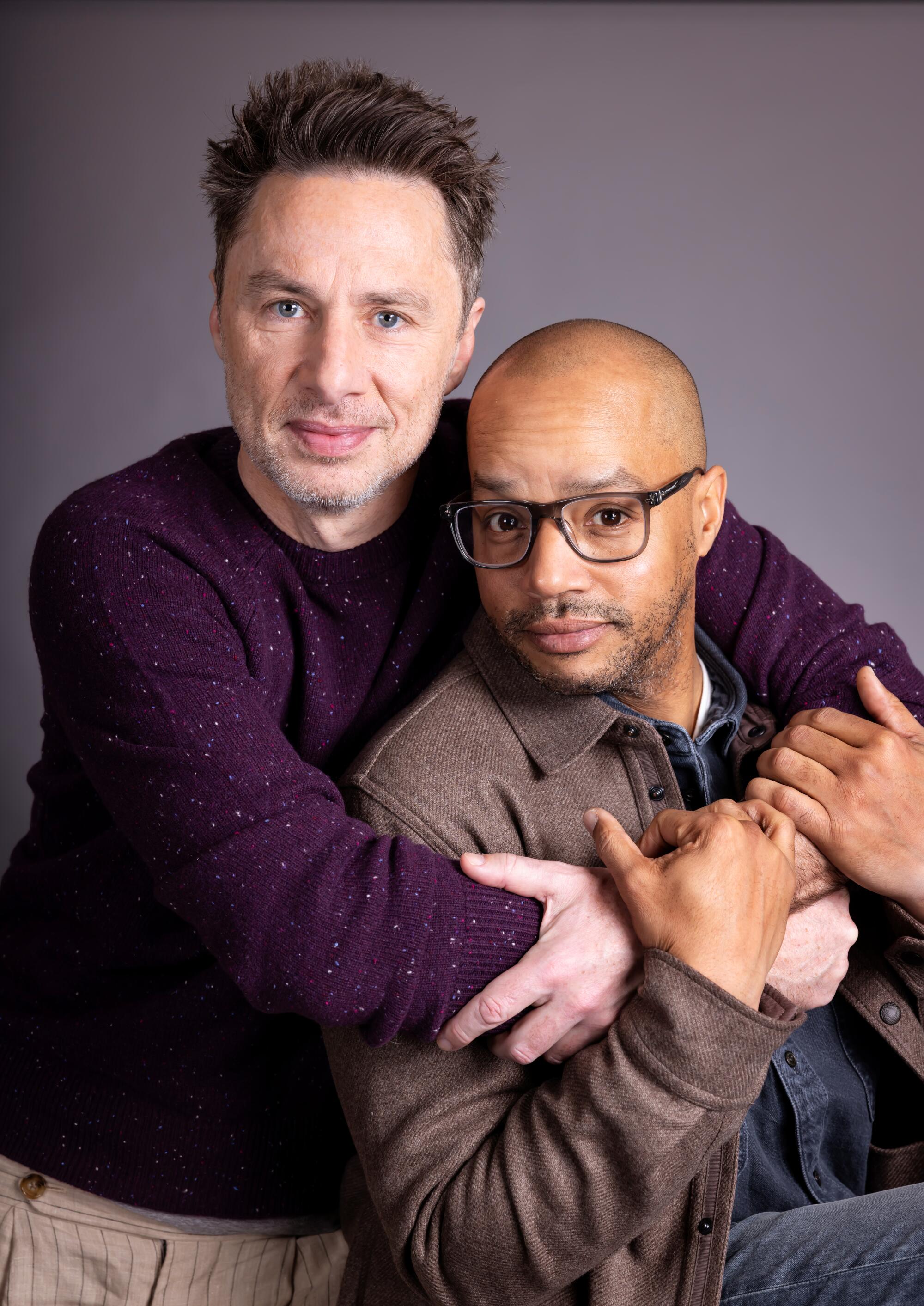 A man in a purple sweater embraces a man in a brown jacket seated next to him.