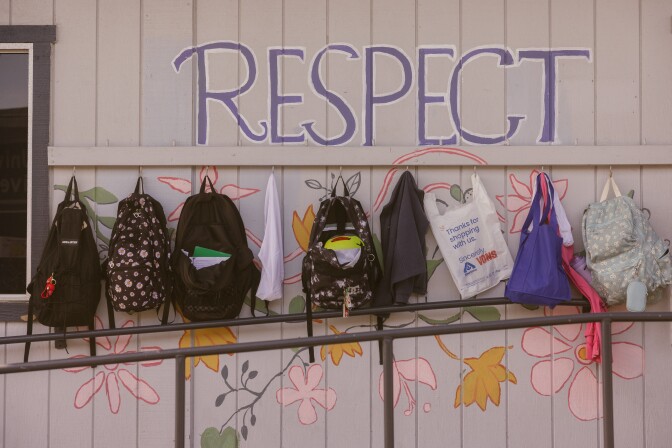A facade of a trailer classroom with a mural of flowers and text that reads "Respect." Along the wall are hooks where various children's bag and backpacks hang.