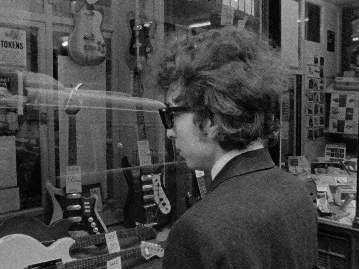 A man in shades looks at guitars in the window.