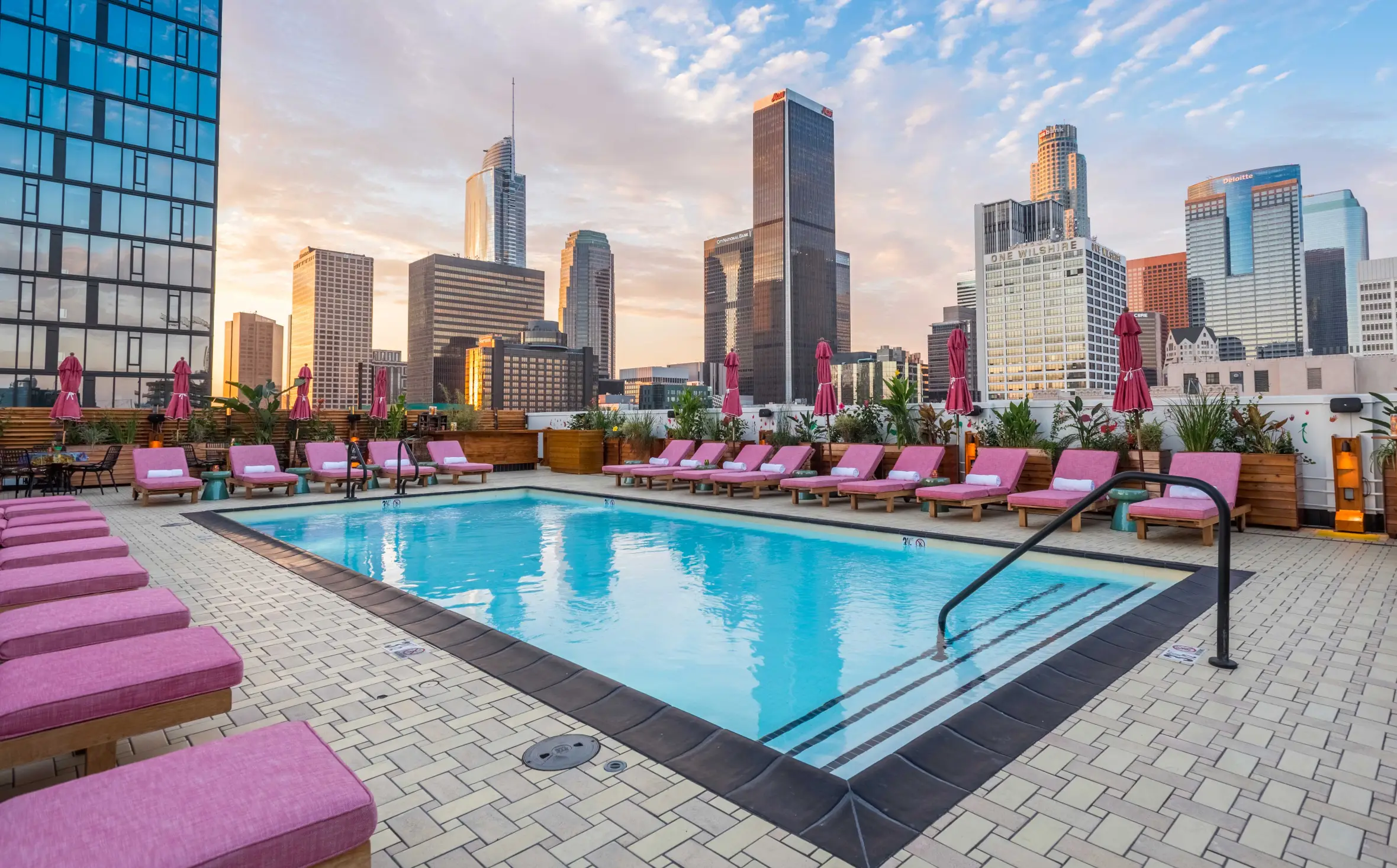 Rooftop pool deck with pink lounge chairs and city skyline.