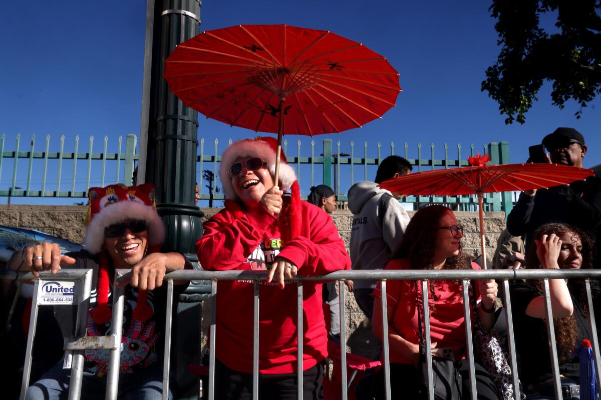People dressed in red and holding up red umbrellas watch a parade.