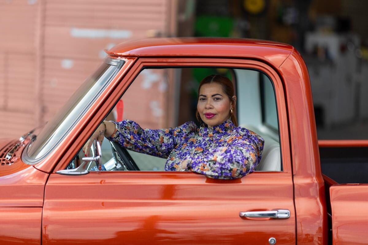 A woman smiles at the camera, framed by the window of her vintage truck.