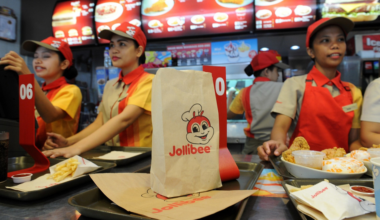 A paper bag with the Jollibee logo sits on a tray on a counter in a fast food restaurant.