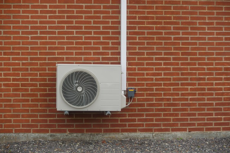 A gray heat pump mounted on red brick wall.
