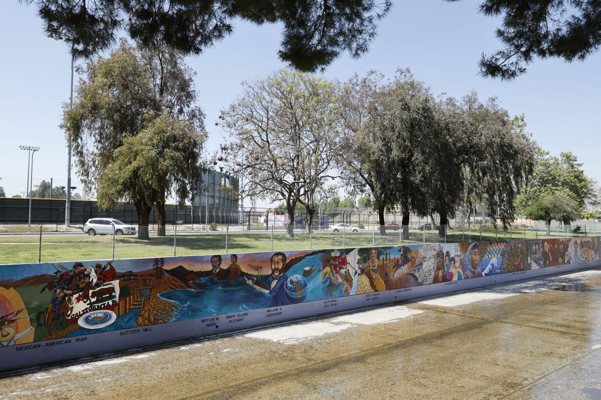 A mural on a flood water channel wall below a grassy areas with trees.