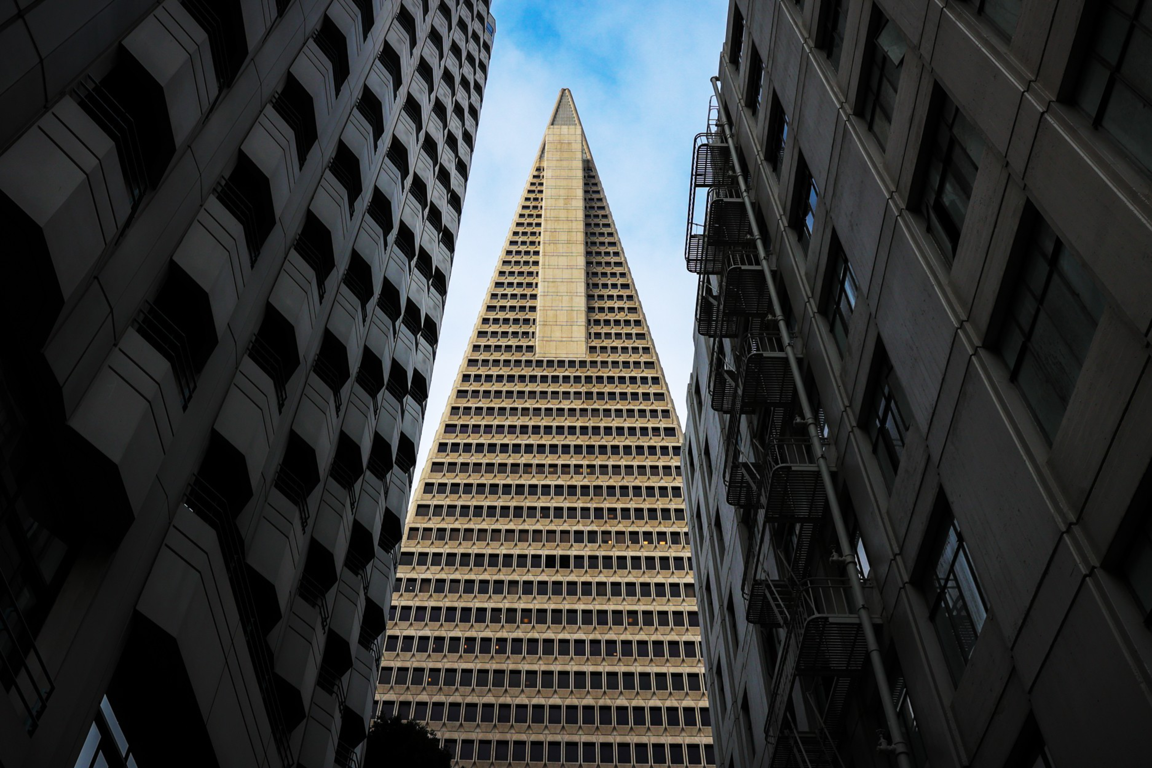A towering skyscraper flanked by two buildings under a blue sky, viewed from a low angle.