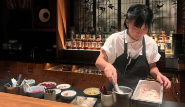 A Flock license plate reader behind a row of shrubs near the entrance of L.A. State Historic Park. A car drives past the park in the background.