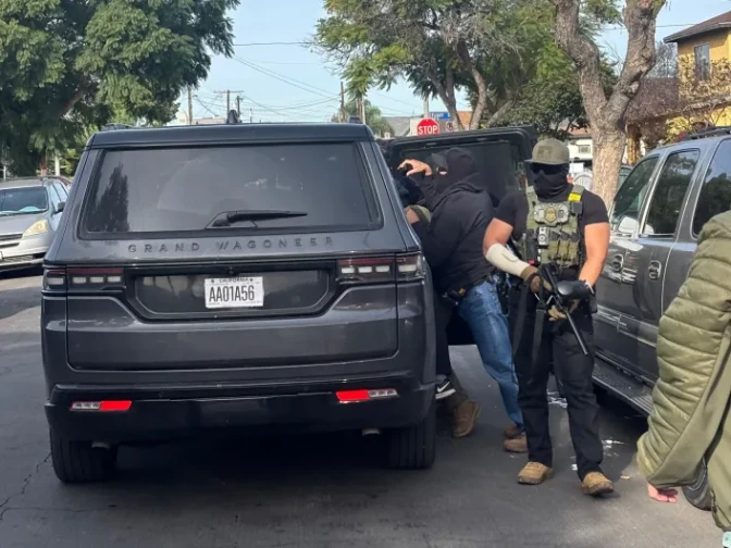 Federal agents stand outside a black SUV as they put a person inside it.