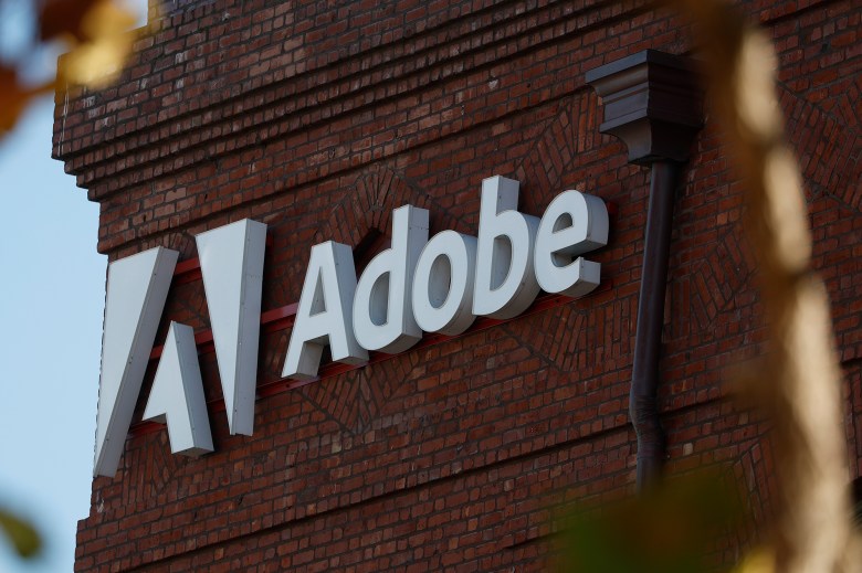 An exterior of a red brick building with a white logo that reads “Adobe” on the wall.