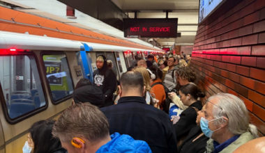 A crowded subway platform at 12th St/Oakland with many people waiting beside a train displaying a "NOT IN SERVICE" sign.
