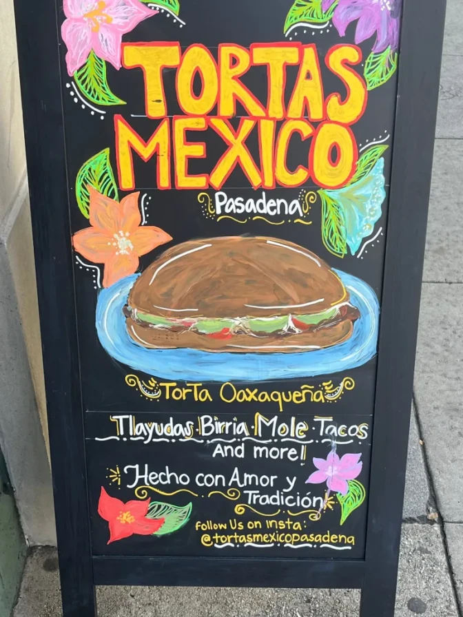 A chalkboard with text and illustrations drawn on it, including one of a torta on a plate. Text written on the board includes "Tortas Mexico. Pasadena."