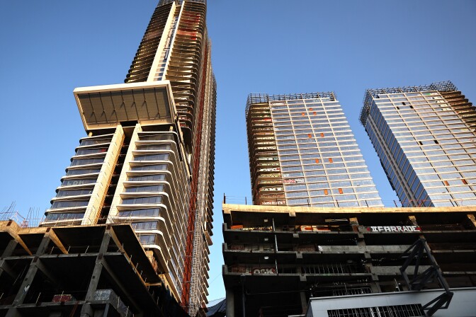Three high-rise buildings under construction, with exposed concrete and scaffolding, set against a clear blue sky.