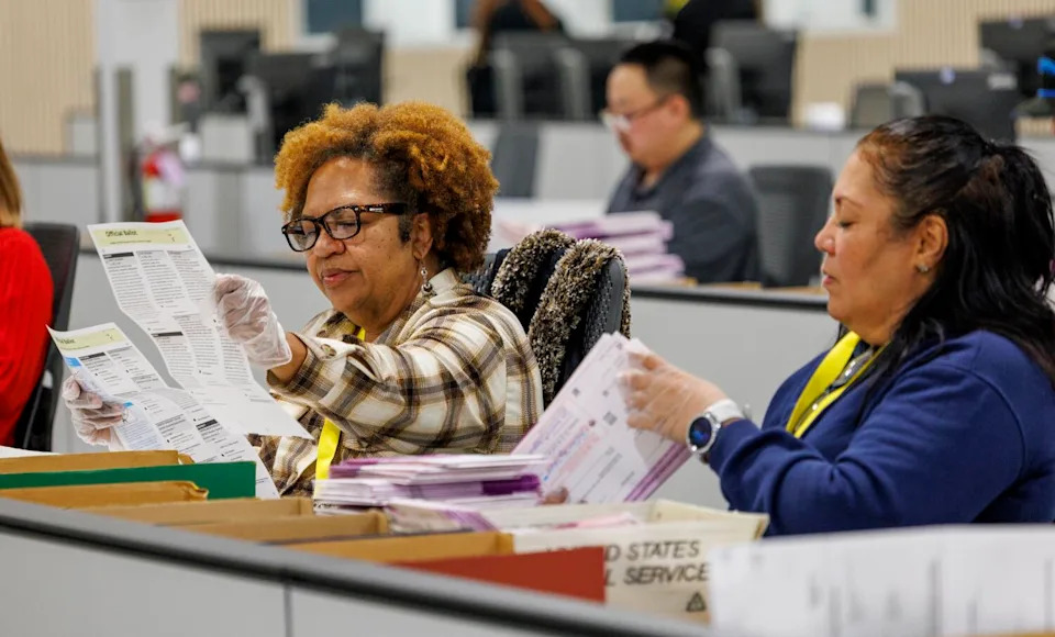 Election workers inspect ballots after extracting them from envelopes.