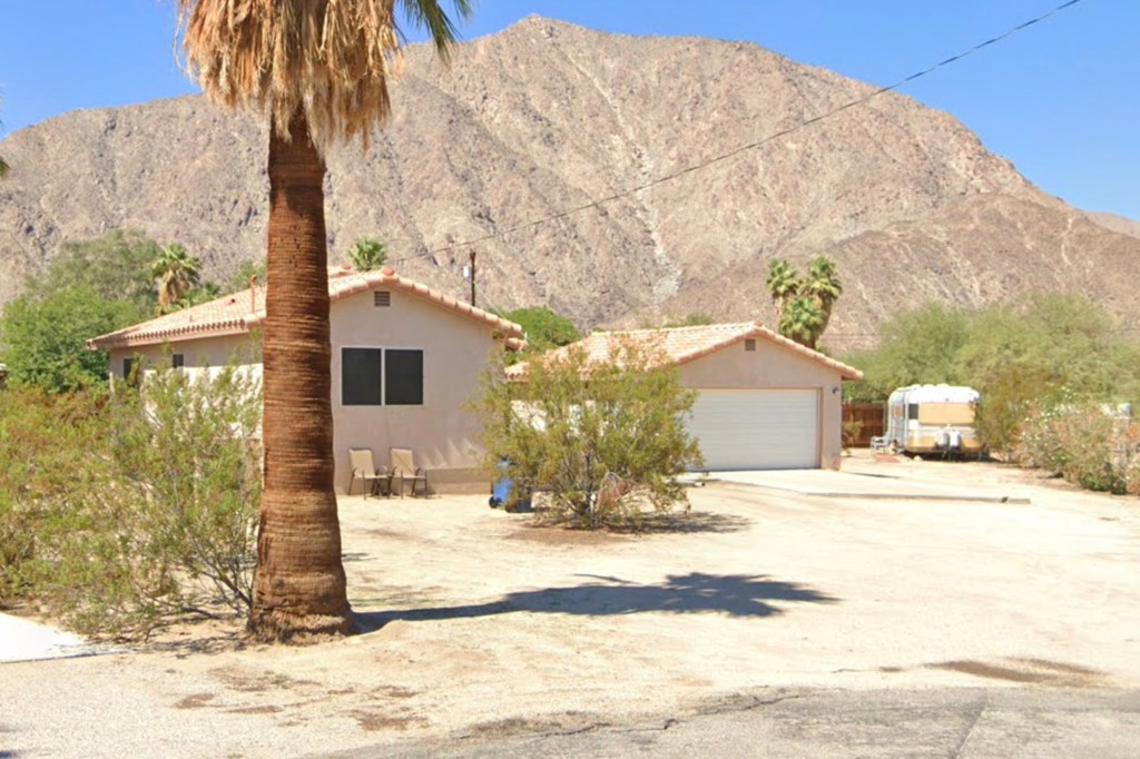 A house with a palm tree in the front, and a large mountain in the background.