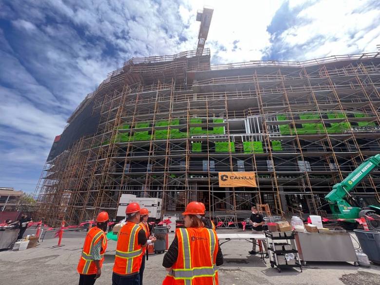 Workers in vests and hard hats stand in front of a construction site for affordable housing.