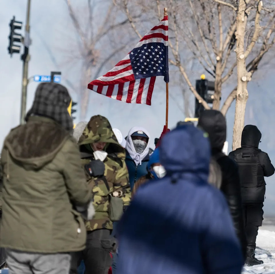 Protesters raise an inverted American flag as law enforcement officers launch tear gas canisters in Minneapolis.