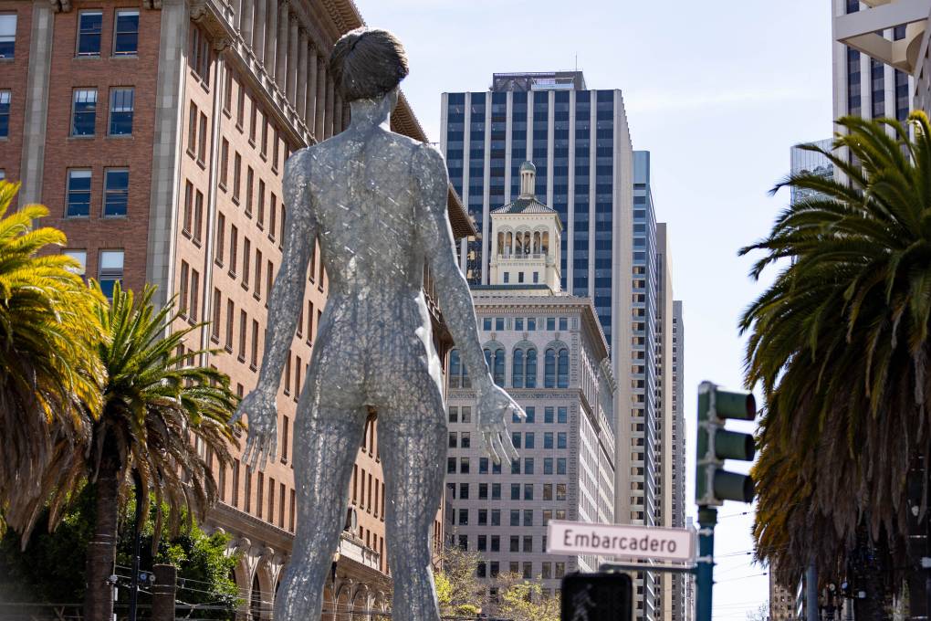 view of backside of giant metal sculpture of nude woman, looking down Market Street