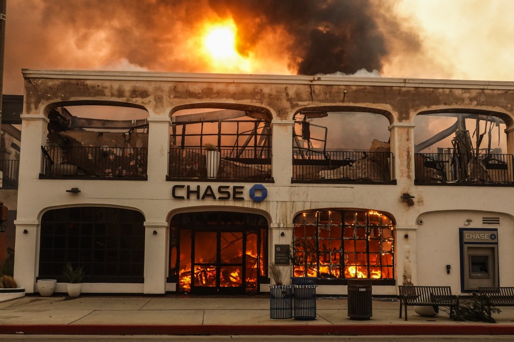 A Chase bank building consumed by fire with orange smoke and flames billowing out of its windows and doors.