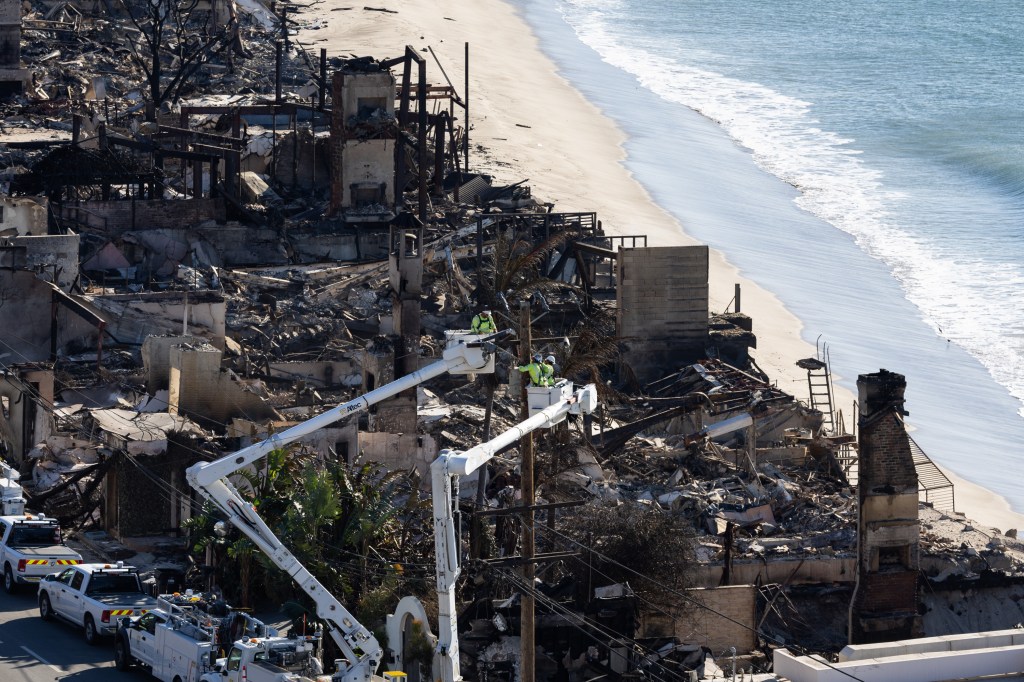 Technicians in bucket trucks conduct maintenance at an electric facility amidst the ruins of beachfront structures after wildfires in Los Angeles.