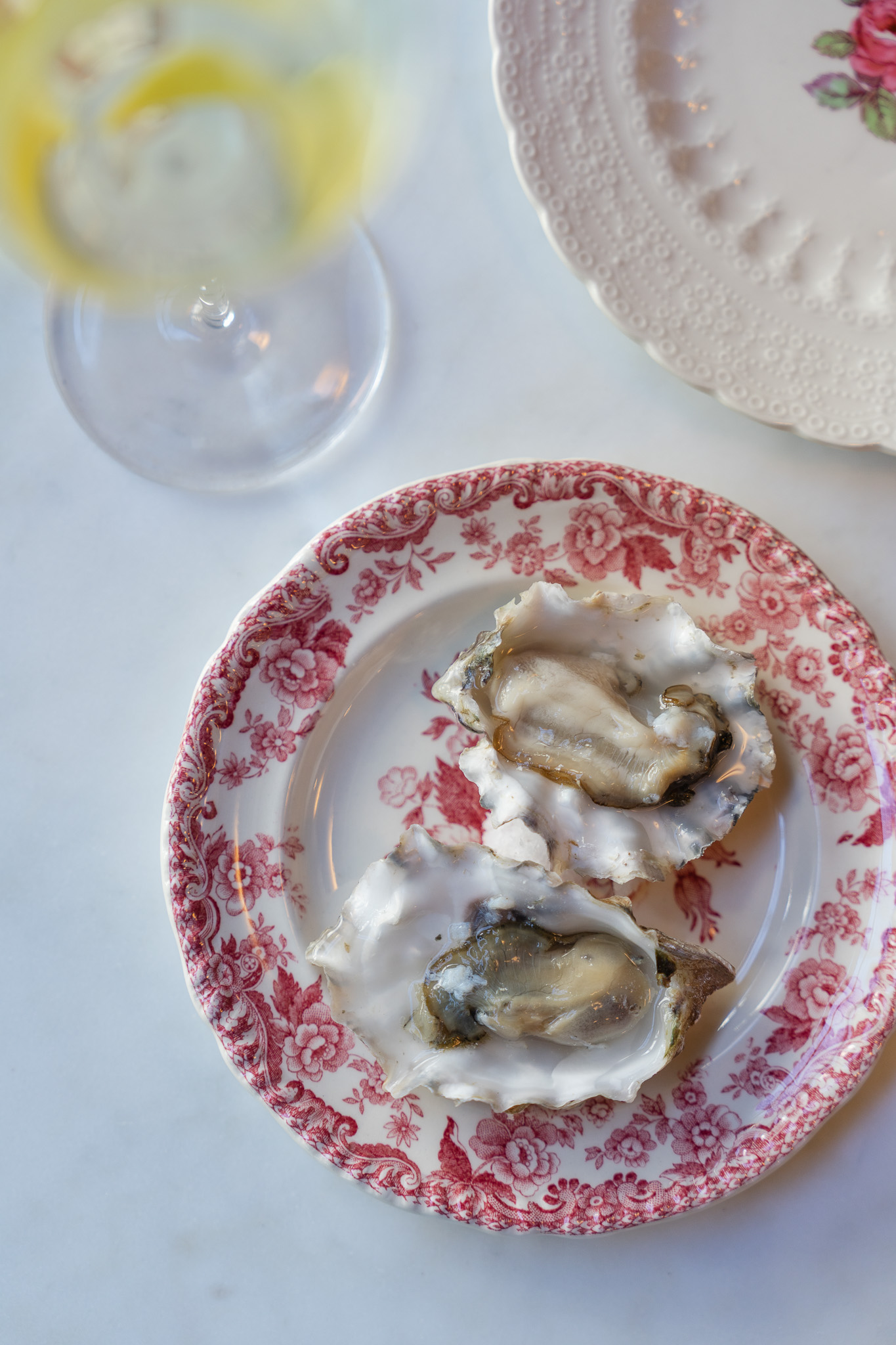A red and white plate with two oysters sits next to a martini with a lemon peel at Frankie’s in San Francisco.