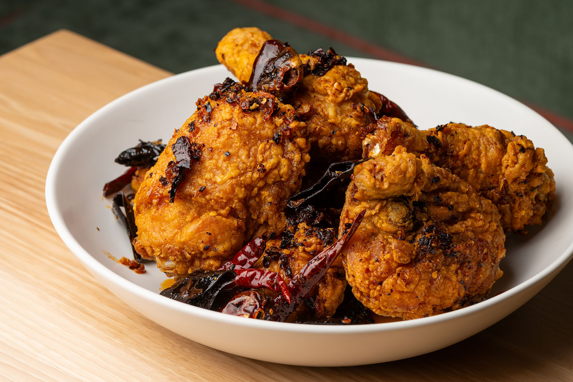 Fried Chongqing chicken drumsticks in a shallow bowl on a light wood table