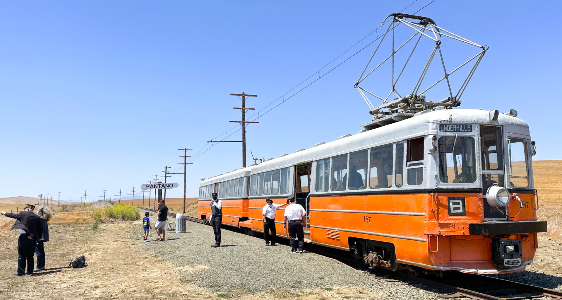 A two-car, orange-and-silver electric train shown in a rural setting at the Western Railway Museum in Solano County.