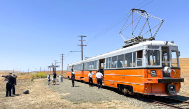 A two-car, orange-and-silver electric train shown in a rural setting at the Western Railway Museum in Solano County.