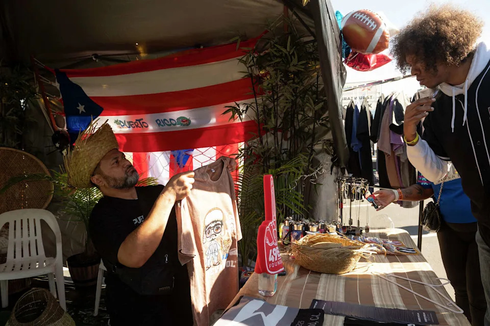 An employee of Puerto Rican Street Cuisine sells merchandise ahead of the game during a Super Bowl fan zone and watch party at the Henry J. Kaiser Center for the Arts in Oakland on Sunday. (Laure Andrillon/For the S.F. Chronicle)