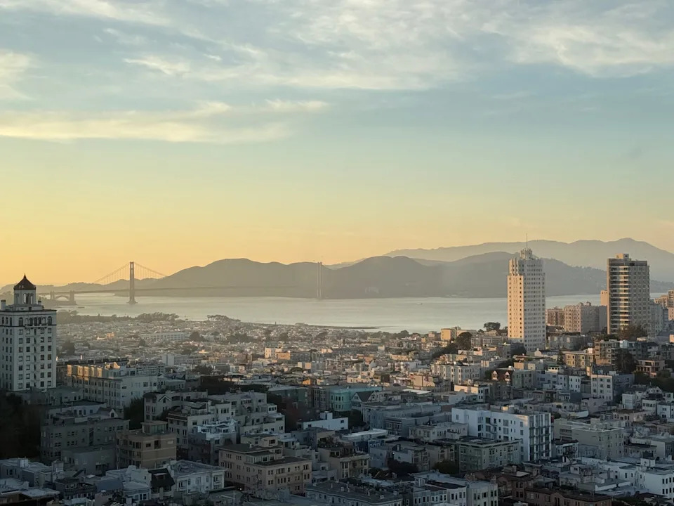Cityscape featuring bay and bridge at sunset.