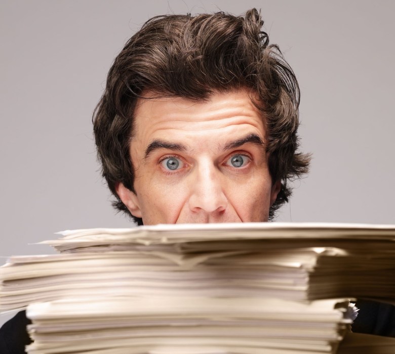 A man peers over the top of a stack of papers