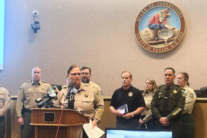 Shannan Moon wearing a sheriff uniform while speaking into a microphone and standing at a podium.