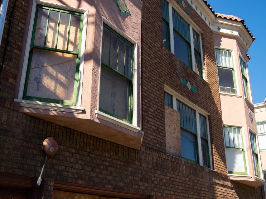 A brick and stucco apartment building with several windows boarded up with plywood during daytime.