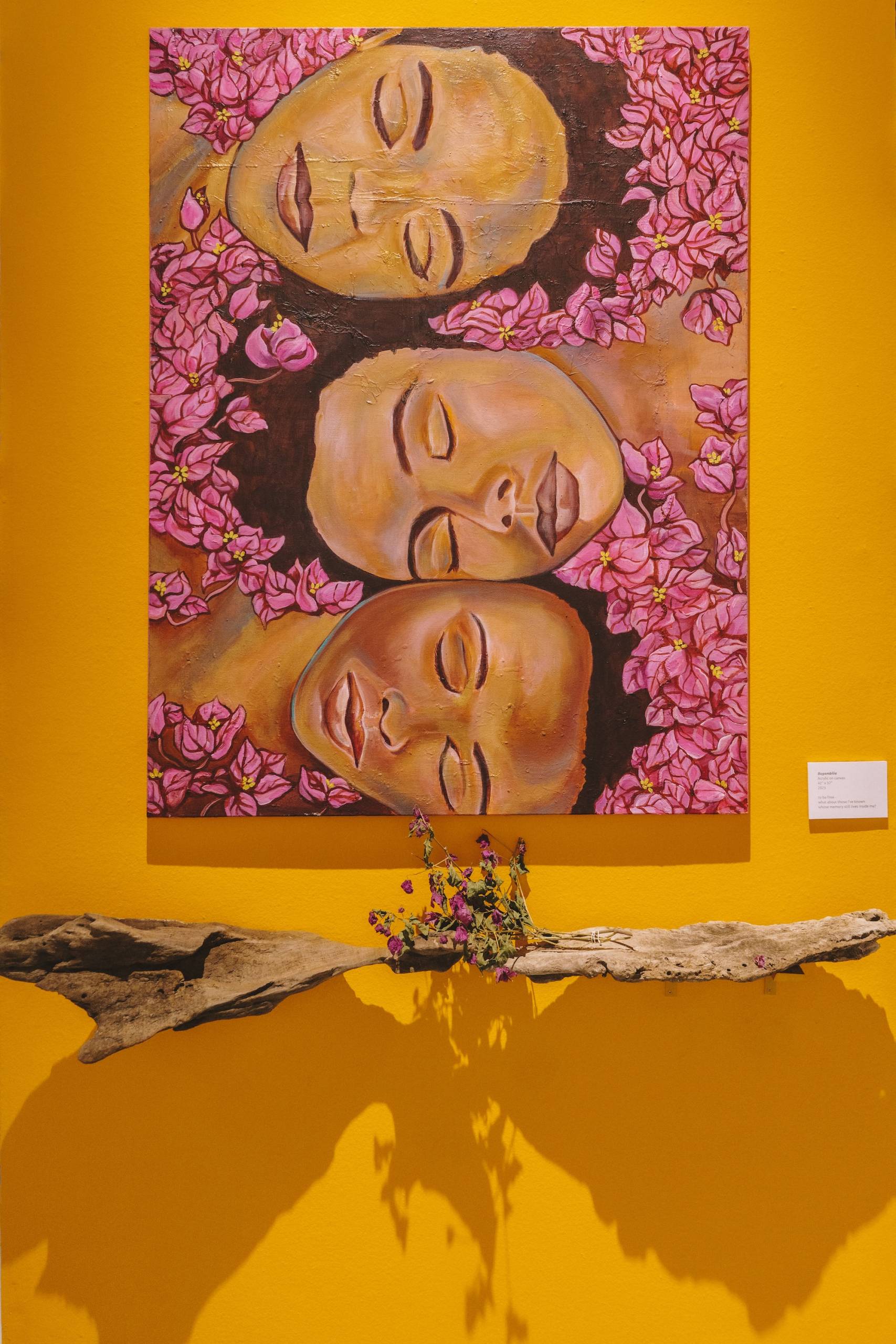 A painted image of three brown-skinned faces, all with their eyes closed, next to each other as they're surrounded by pink flower pedals. 