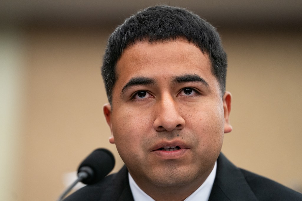 A man in a suit jacket and white shirt speaking into a microphone.