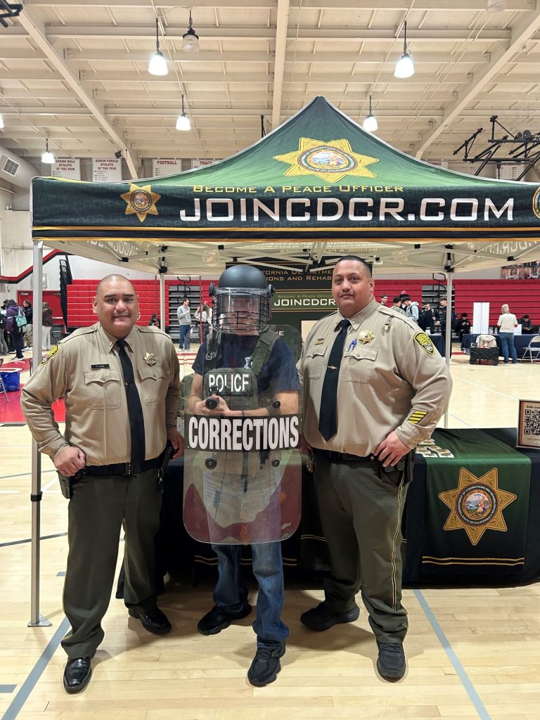 student dressed in corrections tactical gear next to two correctional officers