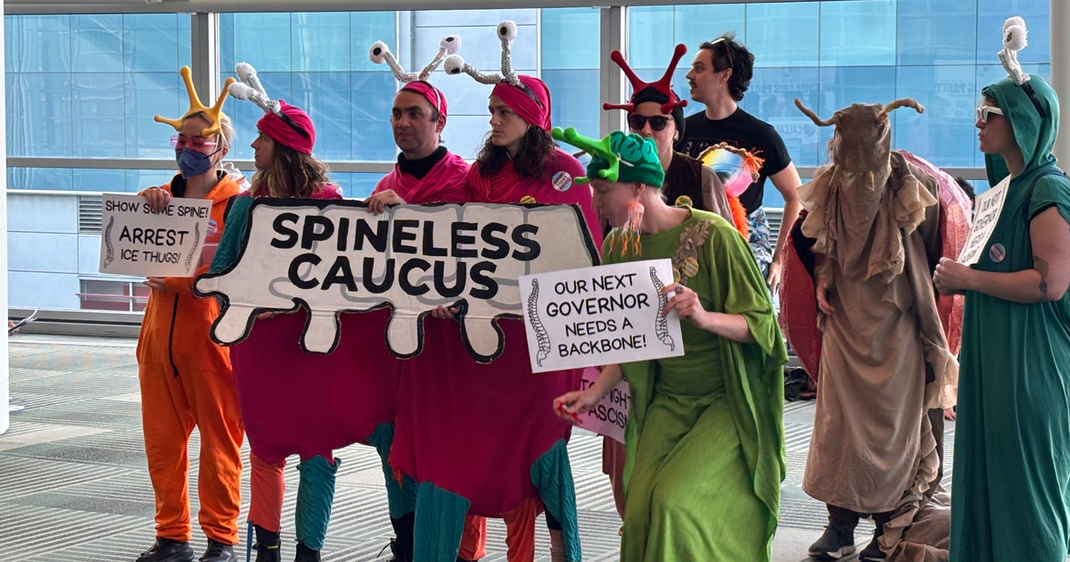 A group dressed as colorful snails and insects hold signs reading "SPINELESS CAUCUS," "ARREST ICE THUGS," and "OUR NEXT GOVERNOR NEEDS A BACKBONE!"