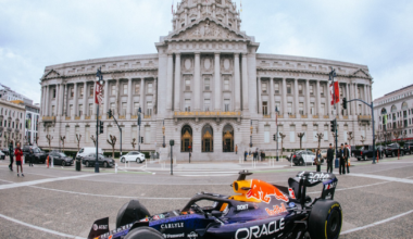 A Red Bull Formula 1 car with Oracle branding is parked on a city street in front of a large neoclassical building with a domed roof.