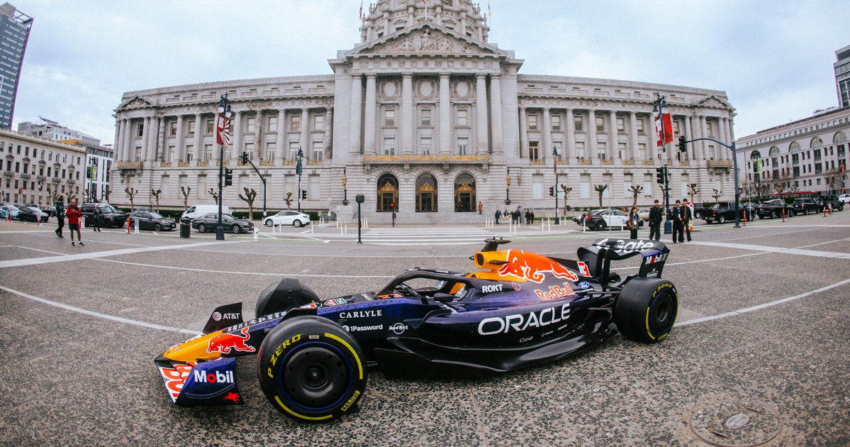 A Red Bull Formula 1 car with Oracle branding is parked on a city street in front of a large neoclassical building with a domed roof.